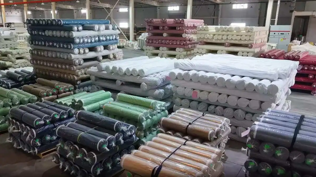 Rolls of finished polyester fabric in different colors stacked in the Perfectextile warehouse